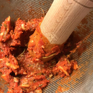 tamizar la salsa de tomate con un colador y una mano de mortero
